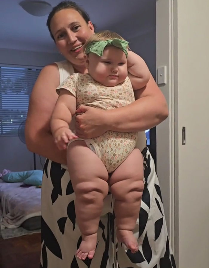 Woman holding giant baby with chubby legs indoors, highlighting rise in giant baby births and related health concerns.