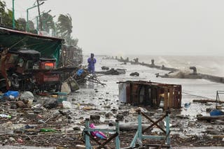 A man stands near debris on a waterfront road amid heavy rain due to weather patterns from Super Typhoon Ragasa in Aparri town, Cagayan province