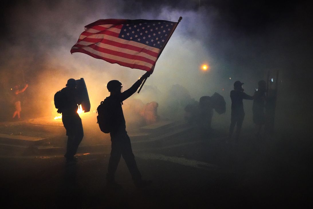 A protester flies an American flag on July 21, 2020, while walking through tear gas fired by federal officers during a protest in Portland.
